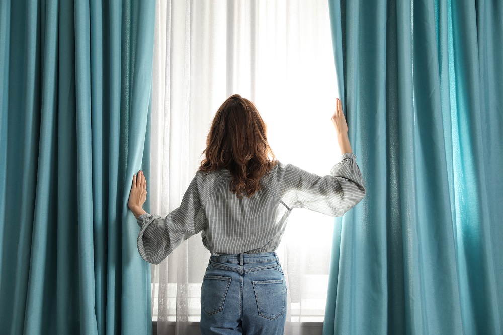 Woman opening window curtains at home